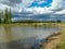 A fish pond, in the water of which there are colorful cumulus clouds and trees, there are recently dug gravel piles on the shore