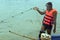 A fisher man is standing on his boat with a pile of fishing net.