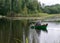 A fisherman in a boat, calm lake water surface, tree reflections, cloudy day, fishing concept