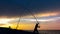 Fisherman cast fishing rods on the seashore at a dramatic sunset. Fisherman silhouette. Night fishing with illuminated