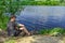 A fisherman catches fish sitting on the shore, against the backdrop of a rural landscape with a river on a sunny spring-summer day