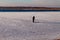 Fisherman figure on little, natural, frozen winter river, makes ice hole with a hand ice auger, man`s silhouette in warm clothes.