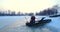 Fisherman fishing from hole in lake from his boat at winter