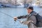 A fisherman with a fishing rod and a backpack catches fish on the bank of a snow-covered river in early spring