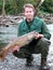 Fisherman holding large salmon fish with river and woods in back