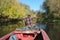 Fisherman with paddle floats down river with dense vegetation along banks