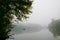 Fisherman in a rubber boat fishing with rods on a small lake, still water surface, reflection and deep fog on an autumn morning