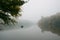 Fisherman in a rubber boat fishing with rods on a small lake, still water surface, reflection, deep fog on a cold autumn morning