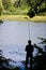 Fisherman`s figure with  a fishing rod on a bank of little natural lake in forest, calm breeze on water surface