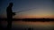 Fisherman silhouette spinning fishing reel during biting at evening sunset