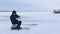 Fisherman sits on frozen river and catches fish then he puts winter fishing rod on ice and pours himself hot tea from thermos