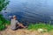 Fisherman sitting on the ground fishing in a pond - top view. Young adult man with fishing rod fishing from the shore on a