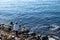 Fisherman standing on rocks with two fishing rods. Blue sea background, above view