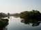 A fisherman is standing on the suspension bridge. Vegetation is reflected in calm water