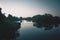 A fisherman is standing on the suspension bridge. Vegetation is reflected in calm water