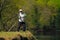 Fisherman throwing the bait into river standing on river bank with green forest in background