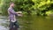 A fisherman throws a fishing rod standing knee-deep in the water of the river. Fly fishing for trout. Summer holidays