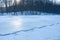 Fisherman trace path on uneven snow surface of frozen lake shore after thaw, winter forest edge sunset, deep shadows, outdoor