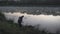 Fisherman tries to save his rod from the grass in front of beautiful foggy lake