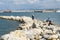 The fisherman in a vest and a hat fishing on stones in sea waves