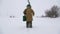 A fisherman walks on a snow-covered lake in search of a good fishing place.