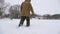 A fisherman walks on a snow-covered lake in search of a good fishing place.