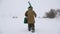 A fisherman walks on a snow-covered lake in search of a good fishing place.