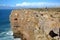 Fishermen angling above the high cliffs at Sagres Fortress Fortaleza with Cabo de Sao Vicente lighthouse in the background