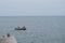 Fishermen with rods dressed in protective vests sitting with backs to viewer in black rubber boat on background of sea horizon