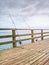 Fishers rods against handrail of wooden bridge. Fishing on harbor mole. Overcast day