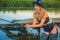 Fisherwoman in a leather swimsuit and a hat is fishing with a fishing rod while standing in the water in rubber boots.