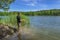 Fishing. Angler with float pole rod catch fish on on beautiful lake at green forest. Fisherman in action, man stand in water