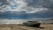 Fishing boat lying in the sand on the shore of the lake, clouds running across the sky. there is nobody around.