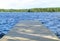 The fishing pier at the lake in rural Finland. Wooden pier at blue water and green forest on sunny day. Wooden jetty bridge