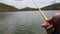 Fishing rod in hand on the background of the lake. Selective focus on the fisherman`s hand. Fishing rod, lake and mountains withou