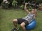 A fit asian male in his early 50s exercising outdoors, doing dumbbell presses on a stability ball