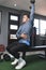 A fit athletic asian guy in a sweatshirt does seated overhead dumbbell one arm tricep extensions. Working out and training triceps