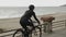 Fit athletic cyclist is spinning pedals on road bike on promenade against beautiful seashore. Young female athlete is pedaling on