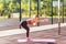Fit athletic woman in tight pants warming up on mat outdoor summer day, doing split or lunge squat exercise