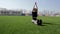 Fit attractive young active woman does yoga stretch pose on huge stadium green grass meditating calmly on warm sunny day