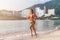 Fit female athlete wearing bikini running on beach with sun shining in camera and hotel resort hills in background
