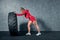 Fit female athlete working out with a huge tire. Side view. Sportswoman doing an strength exercise training.