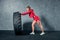 Fit female athlete working out with a huge tire. Side view. Sportswoman doing an strength exercise training.