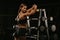 A fit girl in a black suit is leaning on barbells rack after a workout in a gym