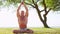 Fit and handsome man practicing yoga outdoor on the grass. Sea, sky and the tree on the background. Stretching exercise