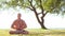 Fit and handsome man practicing yoga outdoor on the grass. Sea, sky and the tree on the background. Stretching exercise