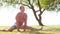 Fit and handsome man practicing yoga outdoor on the grass. Sea, sky and the tree on the background. Stretching exercise