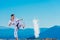 Fit karate athlete kicking a cup filled whit flour causing a big splash while wearing a white kimono on top of a mountain on a