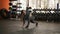 Fit longhaired woman practicing yoga or stretching exercise in bright empty gym studio with dumbbells on background