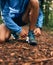 Fit male jogger ties shoes while day training for cross country forest trail race in a nature park.